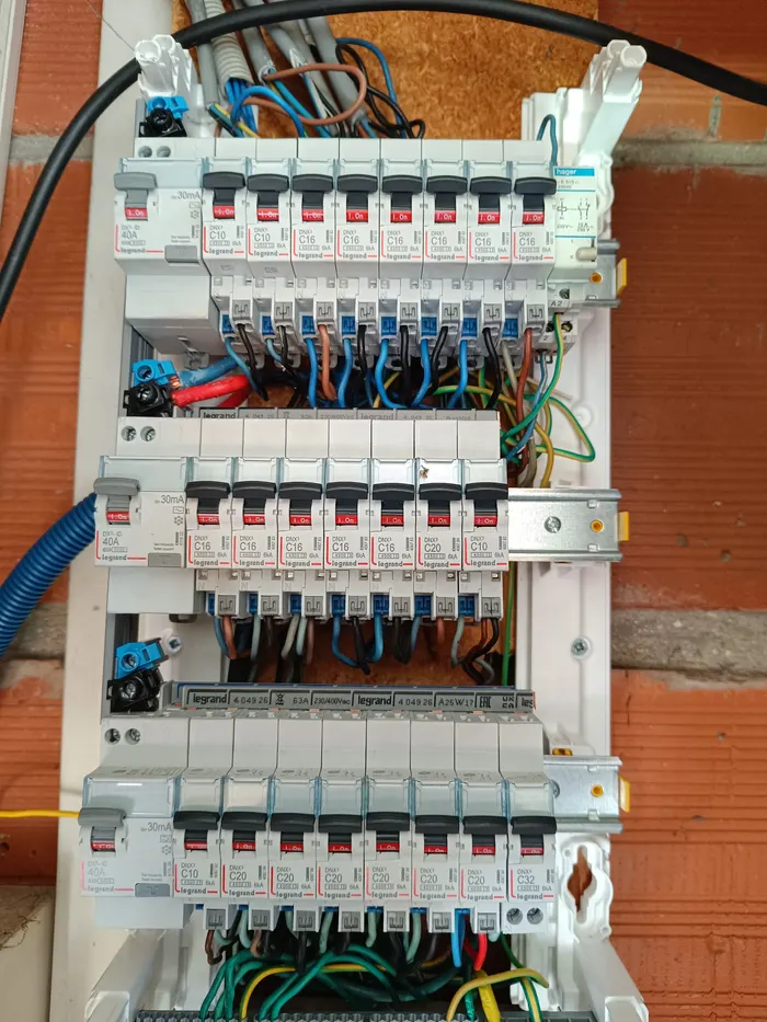 Tableau électrique ouvert : disjoncteurs et câblage, sur un mur de briques